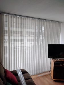 Cortina vertical solar screen de color [Blanco/Gris] instalada en un ventanal moderno, mostrando sus láminas giratorias que filtran la luz solar.